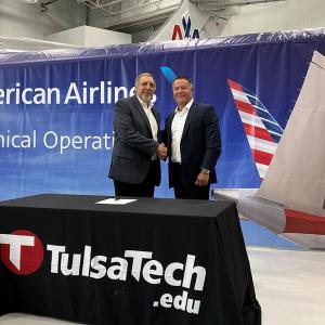 Two people shaking hands in front of an American Airlines banner, behind a Tulsa Tech stand 