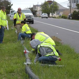 Volunteers working with a drain pipe on the side of a road.