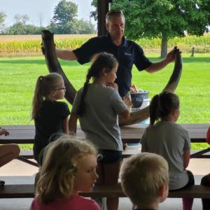 An adult showing a large tusk to a group of children.
