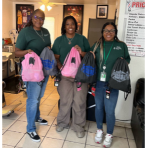 Three smiling people posed holding up small backpack/bags.