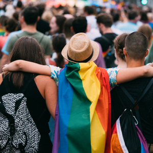 Person with rainbow flag cape embraces two other people