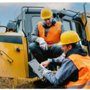 Two people talking, one crouching on a large construction vehicle, the other pointing to something they are holding.