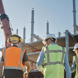 Four construction workers stood in a line looking at a building being built