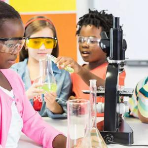a group of children wearing safety glasses, looking at beakers and test tubes