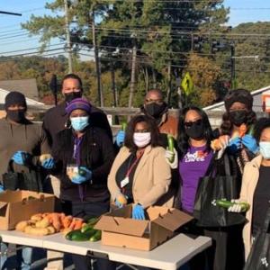 a group of people outside, a table in front of them with fruits and vegetables and boxes