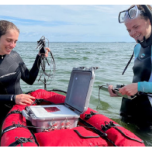 Two people standing in a body of water, devices on a small raft.