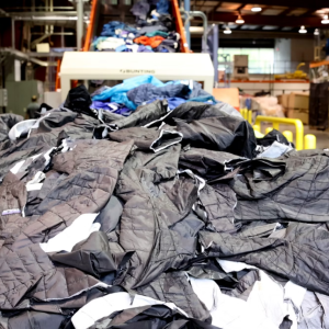 A large pile of waste apparel is loaded onto a conveyor.