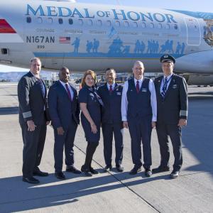 6 people in a line in flight uniforms. The Medal of Honor plane behind them.
