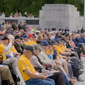 A seated crowd, many wearing the same yellow shirt designating them as a participant in the honor flight program