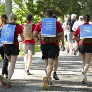A group of runners with a sign on their back "Kohler veterans support safe water for all".