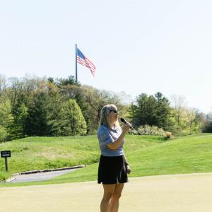 A person standing on a golf course holding a microphone.