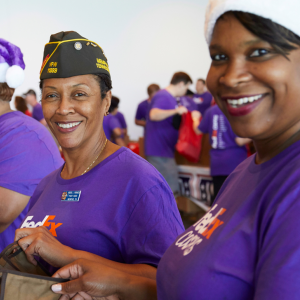two people both wearing FedEx shirts, one has a military hat on