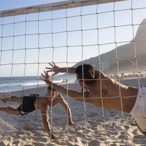 Two people diving for a volley ball on a sand court on a beach.
