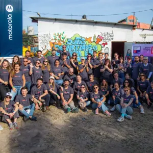 A group of volunteers posed outside a small building. Motorola sign to the side.