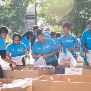 Volunteers packing bags with produce items in large bins outside.