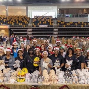 Volunteers posed behind tables of toys in a gymnasium