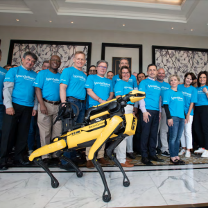 A group with matching shirts behind a yellow robotic dog