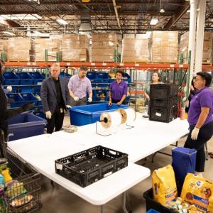 A group of volunteers gathered around a table, listening to one speak.