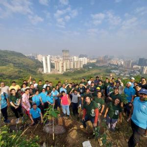 A large group of volunteers posed on a hillside, a city landscape behind them.