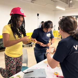 Adult volunteers and children working on building model structures with craft supplies.