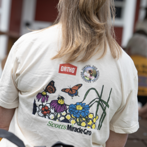 The back of a person's shirt with wildflowers and butterflies and the Ortho and ScottsMiracleGro logos.