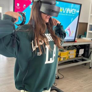 Valeria wearing a VR headset, touching her shoulders. A digital display behind her.