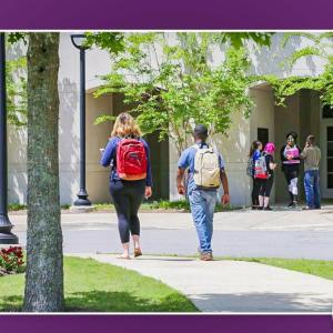 Two students walking on a path to a building where others are standing.