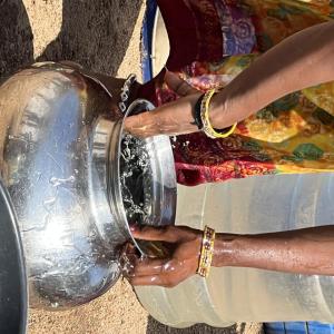 A person bent over washing a metal pot with water.