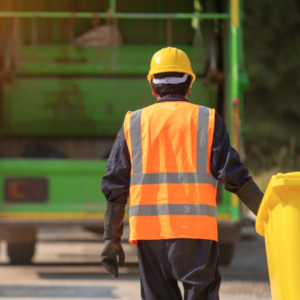 A person bringing a yellow garbage bin towards a garbage truck.