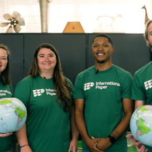 four people stood next to each other wearing green t-shirts, with the people either side holding a globe