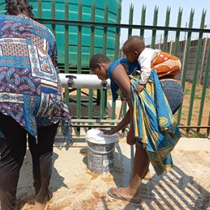 two people collect water, one carrying a child on their back