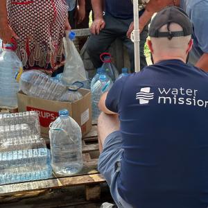 A person in a water mission shirt helping others fill plastic bottles.
