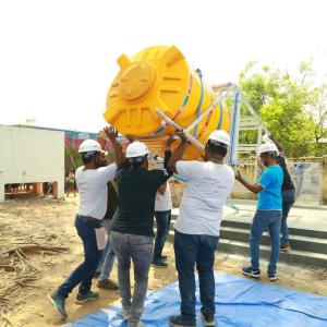 A group of adults in hard harts installing a tall water tank.
