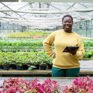 A person holding a tablet and smiling inside a greenhouse