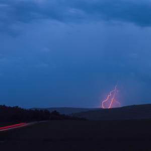 A cloudy sky with red lightning behind a distant hill