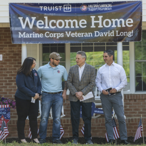 Sgt. David Long and three others stand outside his new home, a banner above them "Welcome Home"