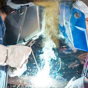 Two people in protective helmets and gloves, welding