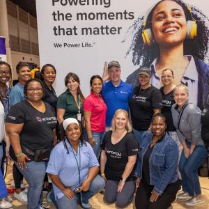 People posed together surrounded by signs "We Power Life" and "Powering Moments That Matter."