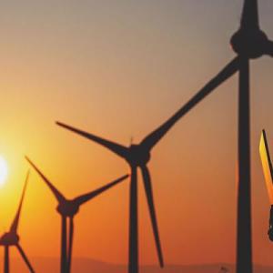 A person on a laptop, a row of wind turbines and a setting sun behind them.