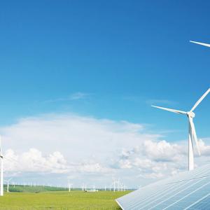 Outside on a bright day, windmills scattered on a large flat plain of grass, a solar panel in the right corner