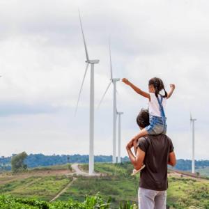 A child one the shoulders of an adult, a row of wind turbines in the distance.