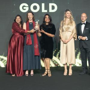Five people on a stage in front of the word "GOLD", three holding an award