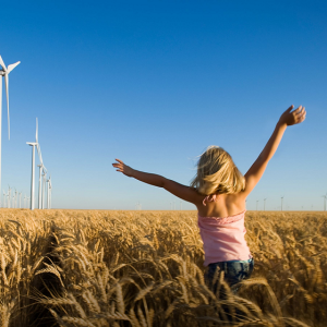 A child running through a crop field. Wind turbines in the distance.