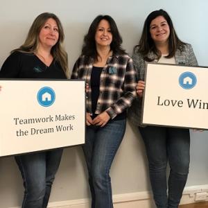 5 women holding signs that read: "Teamwork Makes the Dream Work" and "Love Wins"