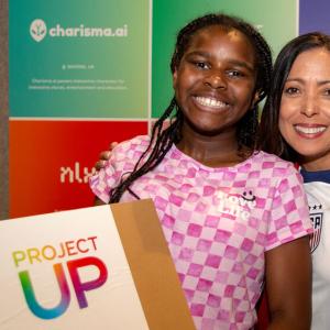 An adult crouched next to a child holding a box with Project Up on it.