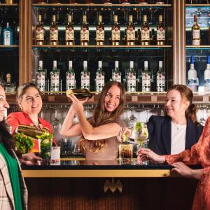 Five women posed in a bar setting with bottles on shelves behind them.