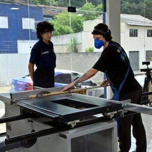 A student working at a wood saw as another looks on.