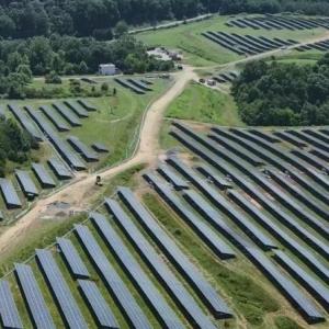 Aerial view of fields of rows of solar panels in a forested area.