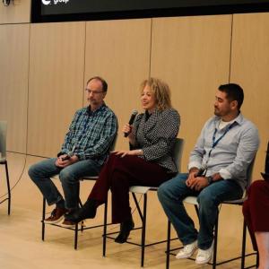 Five people seated at the front of the room, two have microphones.