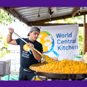 Volunteer cooking a big pot of food with a World Central Kitchen sign behind him 